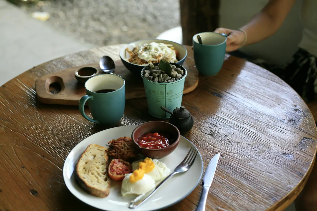 Desayuno servido en mesa redonda de madera: huevo con pan, mermelada y dos tazas de café.